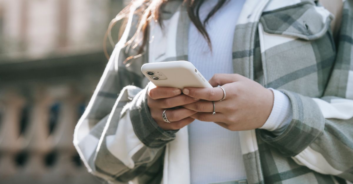 Crop faceless young woman in casual outfit text messaging on phone in city street in daytime